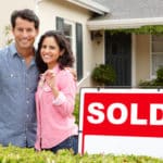 couple in front of home sold sign